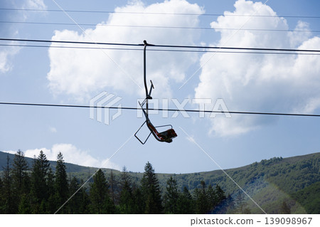 Empty Chairlift Chair Suspended Above a Vibrant Green Mountain Landscape 139098967