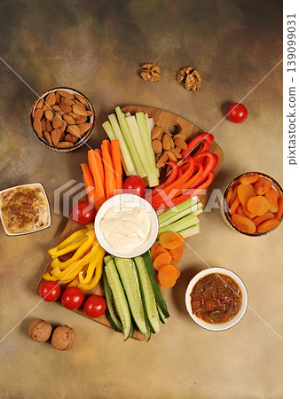 Hummus platter with appetizers, healthy food kitchen background with hummus bowl and raw vegetable sticks, nuts and dried apricots. Middle East plate, traditional vegan appetizers, Hummus platter with appetizers, healthy food kitchen background with hummus bowl and raw vegetable sticks, nuts and dried apricots. Middle East plate, traditional vegan appetizers, 139099031