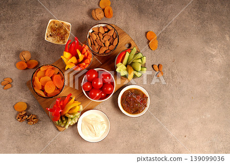 Healthy food kitchen background with hummus bowl and raw vegetable sticks, nuts and dried apricots. Hummus platter with appetizers, Middle Eastern plate, traditional vegan snacks, Healthy food kitchen background with hummus bowl and raw vegetable sticks, nuts and dried apricots. Hummus platter with appetizers, Middle Eastern plate, traditional vegan snacks, 139099036