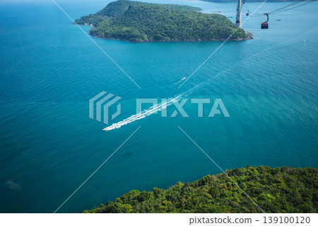 An aerial photograph of a speedboat sailing across the emerald green sea off Phu Quoc Island in Vietnam. An aerial photograph of a speedboat sailing across the emerald green sea off Phu Quoc Island in Vietnam. 139100120