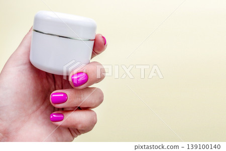 Manicure cosmetics cream skincare hand with pink nails holding white jar for beauty care. Spa moisturizing product scene for skin, cuticle, body care, salon procedure and cosmetic treatment. 139100140