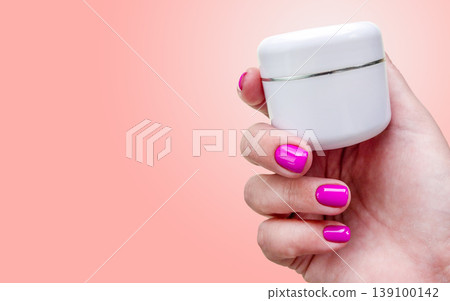 Manicure cosmetics cream skincare hand with pink nails holds white jar on pastel pink background for beauty care. Spa moisturizing product for skin, cuticle, body care, salon procedure and treatment. Manicure cosmetics cream skincare hand with pink nails holds white jar on pastel pink background for beauty care. Spa moisturizing product for skin, cuticle, body care, salon procedure and treatment. 139100142