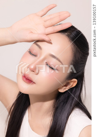 Beautiful Asian woman with clean glowing skin and long black hair posing against a neutral background. Concept of skincare, beauty treatment, and sun protection. 139100157
