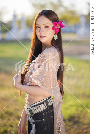 Trendy Thai fashion woman wearing a traditional Sabai paired with denim jeans at temple, reflecting the growing fashion trend in Thailand that blends cultural heritage with contemporary street style. Trendy Thai fashion woman wearing a traditional Sabai paired with denim jeans at temple, reflecting the growing fashion trend in Thailand that blends cultural heritage with contemporary street style. 139100183