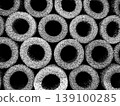 Cylindrical shapes are lined up closely in a dark setting. The shapes have hollow centers and form a pattern that creates depth. The lighting highlights their texture. 139100285