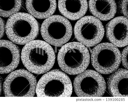Cylindrical shapes are lined up closely in a dark setting. The shapes have hollow centers and form a pattern that creates depth. The lighting highlights their texture. Cylindrical shapes are lined up closely in a dark setting. The shapes have hollow centers and form a pattern that creates depth. The lighting highlights their texture. 139100285