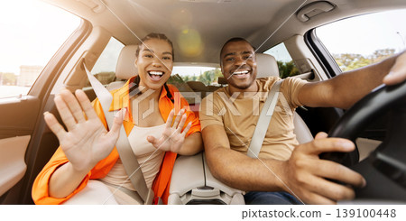 Young black couple waving hands toward camera inside car, expressing excitement Young black couple waving hands toward camera inside car, expressing excitement 139100448