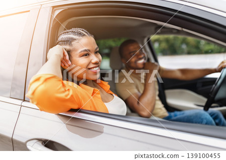 Relaxed black woman leaning out of car window while traveling with partner Relaxed black woman leaning out of car window while traveling with partner 139100455