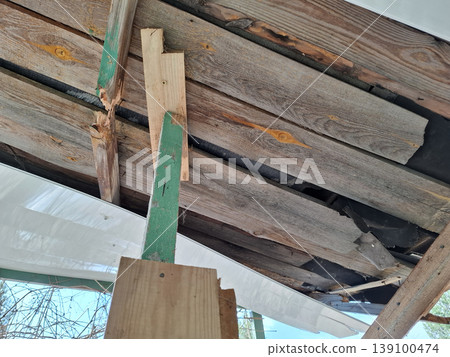 Upward view shows structural repairs on an old wooden roof. New timber supports are placed under green painted beams. Work is in progress to maintain the building's safety. Upward view shows structural repairs on an old wooden roof. New timber supports are placed under green painted beams. Work is in progress to maintain the building's safety. 139100474