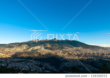 Spectacular panoramic view of Quito, the capital of Ecuador, during a golden sunrise. The sun illuminates the slopes of the majestic Pichincha Volcano and the vast Andean cityscape. Spectacular panoramic view of Quito, the capital of Ecuador, during a golden sunrise. The sun illuminates the slopes of the majestic Pichincha Volcano and the vast Andean cityscape. 139100531