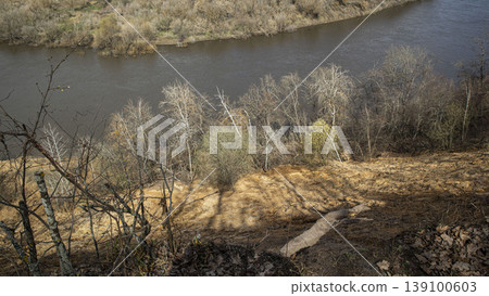 A high angle view shows the Don River winding through Krivoborye in the Voronezh region. Steep sandy banks and sparse early spring plants are visible under soft daylight. A high angle view shows the Don River winding through Krivoborye in the Voronezh region. Steep sandy banks and sparse early spring plants are visible under soft daylight. 139100603
