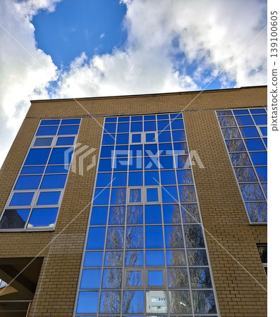 The shot shows a modern brick building from below. The large blue windows reflect the sky and trees around the structure. It captures a clear day with bright clouds. The shot shows a modern brick building from below. The large blue windows reflect the sky and trees around the structure. It captures a clear day with bright clouds. 139100605
