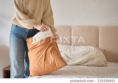 Person putting pillow into pillowcase while making bed in bedroom 139100691