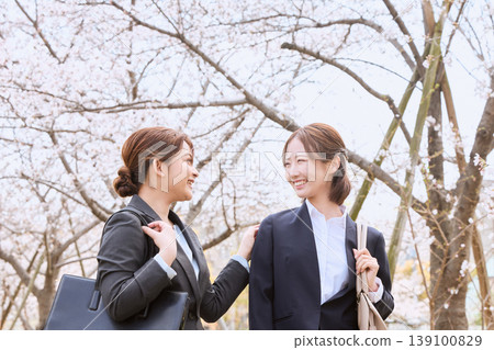 An image of two young women in business suits, new employees, and job-hunting, smiling and chatting under a row of cherry trees. An image of two young women in business suits, new employees, and job-hunting, smiling and chatting under a row of cherry trees. 139100829