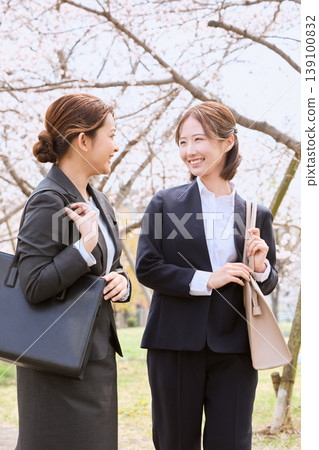 Two female new employees walking under a row of cherry trees; job seekers smiling in business suits; an image of a spring induction ceremony. 139100832