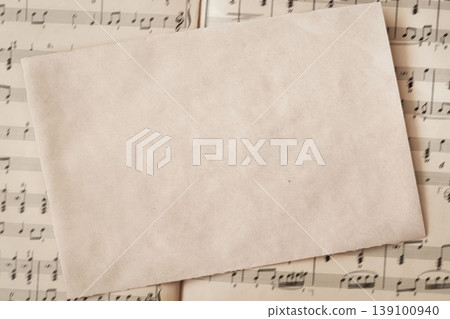 Blank handmade paper sheet placed over music score pages, paper mockup background for invitation, menu or letter design. Music paper composition, vintage texture, copy space paper 139100940