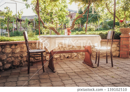 Sunlit Outdoor Table Set For Two With Linen Tablecloth And Mismatched Chairs, Delicate Centerpiece And Morning Coffee Setting, Intimate Terrace Mood For Lifestyle And Hospitality Contexts Sunlit Outdoor Table Set For Two With Linen Tablecloth And Mismatched Chairs, Delicate Centerpiece And Morning Coffee Setting, Intimate Terrace Mood For Lifestyle And Hospitality Contexts 139102510