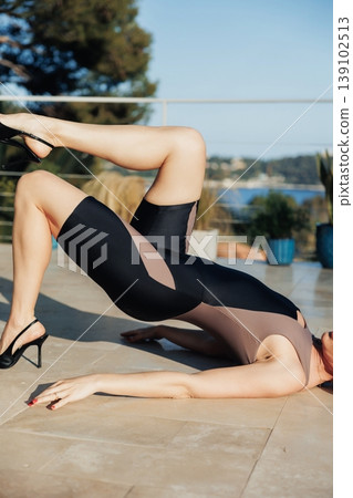 Poolside Elegance White Model Stretching On Deck Near Glass Railing, Heels On And Legs Lifted In Sculpted Pose, Warm Sunlight And Mediterranean Foliage In Background, Editorial Wellness Poolside Elegance White Model Stretching On Deck Near Glass Railing, Heels On And Legs Lifted In Sculpted Pose, Warm Sunlight And Mediterranean Foliage In Background, Editorial Wellness 139102513