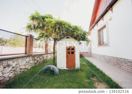 Miniature Garden House With Tiny Door And Climbing Vine, Tucked Into Green Lawn Next To Stone Wall Ideal For Whimsical, Children Play, Fairy Garden And Decorative Outdoor Styling Concepts. Miniature Garden House With Tiny Door And Climbing Vine, Tucked Into Green Lawn Next To Stone Wall Ideal For Whimsical, Children Play, Fairy Garden And Decorative Outdoor Styling Concepts. 139102516