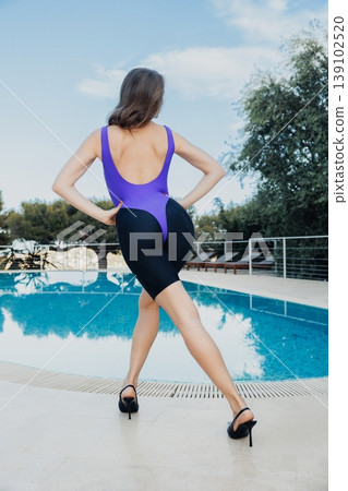 Poolside Confidence White Model Showing Back Profile In Purple Unitard And Heels, Hands On Hips And Strong Posture, Modern Lifestyle Editorial With Bright Terrace Reflections. Poolside Confidence White Model Showing Back Profile In Purple Unitard And Heels, Hands On Hips And Strong Posture, Modern Lifestyle Editorial With Bright Terrace Reflections. 139102520
