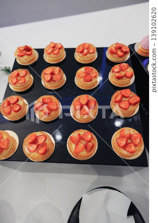 Mini Strawberry Tarts On Black Tray, Bakery Preparing Catering Order, Golden Crusts Filled With Vanilla Cream, Glazed Strawberry Slices, Neat Rows On White Tablecloth, Highangle Studio 139102620