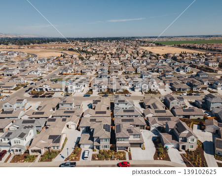 Aerial Planned Grid Community Long Perspective Revealing Symmetric Rows Of Houses, Narrow Backyards, Parked Cars, Distant Farmland, Serene Afternoon Light And Efficient Street Layout. 139102625