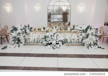 Lavish Floraladorned Wedding Head Table, Set In Elegant Ballroom With White Linens, Abundant Greenery Garlands, Cascading Roses, Crystal Candlesticks, Mirrored Backdrop Reflecting Soft 139102632