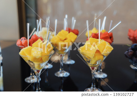 Fresh Pineapple And Watermelon Skewers Presented In Stemmed Glasses On Black Buffet Table, Vibrant Tropical Colors, Cocktail Forks, Perfect For Summer Receptions And Party Catering Fresh Pineapple And Watermelon Skewers Presented In Stemmed Glasses On Black Buffet Table, Vibrant Tropical Colors, Cocktail Forks, Perfect For Summer Receptions And Party Catering 139102727