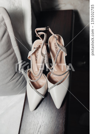White Bridal Heels Placed On Bench, Soft Natural Light Highlighting Satin Straps And Pointed Toes, Subtle Rhinestone Detail, Muted Neutral Palette Evoking Wedding Morning Calm And Elegant White Bridal Heels Placed On Bench, Soft Natural Light Highlighting Satin Straps And Pointed Toes, Subtle Rhinestone Detail, Muted Neutral Palette Evoking Wedding Morning Calm And Elegant 139102785