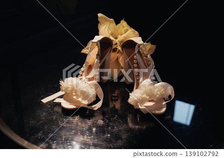 Moody Bridal Shoes With Calla Lilies Arranged On Reflective Glass Table Under Warm Spotlight, Delicate Fabric Flowers And Ribbon Accents, Vintage Satin Texture And Intimate Editorial 139102792
