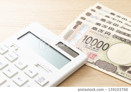 桌上放著一張10000日圓的鈔票和一個計算機。 桌上放著一張10000日圓的鈔票和一個計算機。 139103788