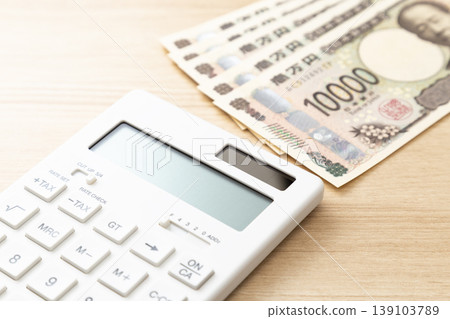 桌上放著一張10000日圓的鈔票和一個計算機。 桌上放著一張10000日圓的鈔票和一個計算機。 139103789
