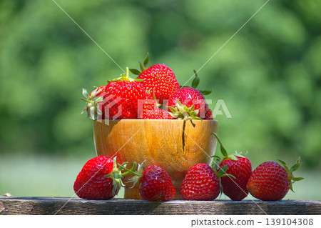 Fresh strawberries overflowing a wooden bowl in a garden Fresh strawberries overflowing a wooden bowl in a garden 139104308