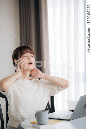 Exhausted asian woman feeling stressed and suffering neck pain during intensive work and study session using technology at home sitting by window seeking relief from physical discomfort Exhausted asian woman feeling stressed and suffering neck pain during intensive work and study session using technology at home sitting by window seeking relief from physical discomfort 139104481