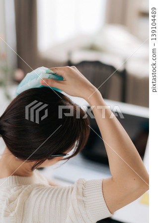 Exhausted asian woman feeling deeply stressed holds cold pack to relieve painful headache while using modern technology for daily work and difficult study at comfortable home desk Exhausted asian woman feeling deeply stressed holds cold pack to relieve painful headache while using modern technology for daily work and difficult study at comfortable home desk 139104489