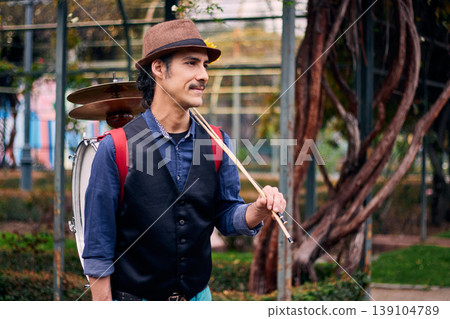 Adult man with a mustache, dressed formally and colorfully, posing and playing a bass drum on his back, Chilean chinchinero, street musician who plays the bass drum and dances in the streets Adult man with a mustache, dressed formally and colorfully, posing and playing a bass drum on his back, Chilean chinchinero, street musician who plays the bass drum and dances in the streets 139104789