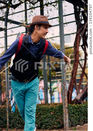 Adult man with a mustache, dressed formally and colorfully, posing and playing a bass drum on his back, Chilean chinchinero, street musician who plays the bass drum and dances in the streets Adult man with a mustache, dressed formally and colorfully, posing and playing a bass drum on his back, Chilean chinchinero, street musician who plays the bass drum and dances in the streets 139104797