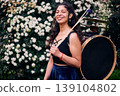 Beautiful dark-haired Latina woman posing with a drum and cymbals on her back, full of joy, a chinchinera, a street musician who dances and plays her drum in the streets. Chilean heritage 139104802