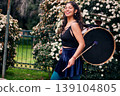 Beautiful dark-haired Latina woman posing with a drum and cymbals on her back, full of joy, a chinchinera, a street musician who dances and plays her drum in the streets. Chilean heritage 139104805