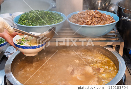 一家牛肉拉麵店的廚房場景，展示了從製作麵條到擺盤的烹飪過程。 139105794