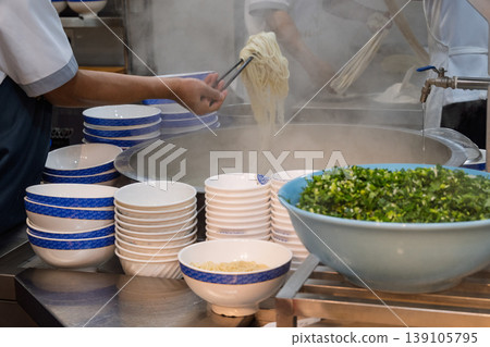 一家牛肉拉麵店的廚房場景，展示了從製作麵條到擺盤的烹飪過程。 139105795