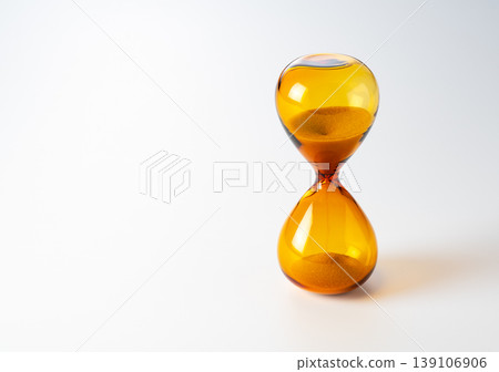 Amber-colored hourglass placed against a white background 139106906