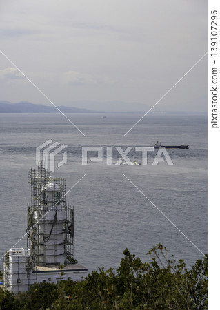 The Sada Cape Lighthouse, under construction, stands on the top of the cape, and the rock face contains a cave. 139107296