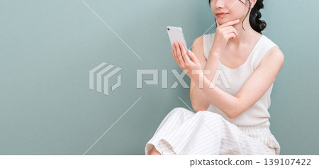 一位年輕的亞洲女性在家中看著智慧型手機,若有所思(擔憂、嚴肅、思考、計劃) 一位年輕的亞洲女性在家中看著智慧型手機,若有所思(擔憂、嚴肅、思考、計劃) 139107422
