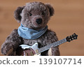A teddy bear holding a guitar; dark brown bear, brown guitar; close-up. 139107714