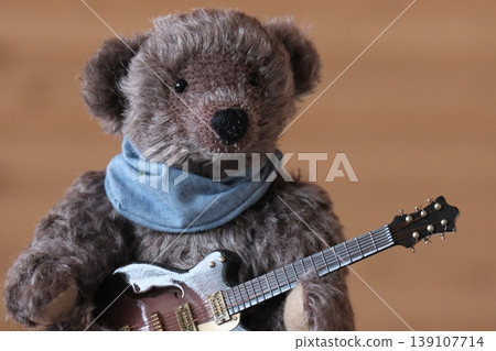 A teddy bear holding a guitar; dark brown bear, brown guitar; close-up. A teddy bear holding a guitar; dark brown bear, brown guitar; close-up. 139107714