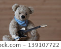 A teddy bear holding a guitar; beige bear, beige guitar; slightly close-up; space on the right. 139107722