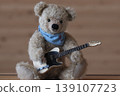 A teddy bear holding a guitar; beige bear, beige guitar; a close-up shot. 139107723