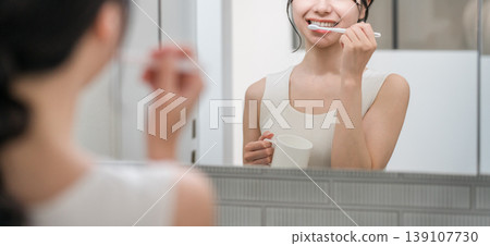 Young Asian woman brushing her teeth while looking in the mirror in the bathroom Young Asian woman brushing her teeth while looking in the mirror in the bathroom 139107730