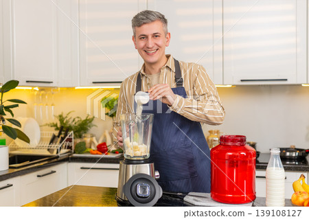 Middle-aged man pouring protein powder into blender for healthy shake meal prep in kitchen at home Middle-aged man pouring protein powder into blender for healthy shake meal prep in kitchen at home 139108127